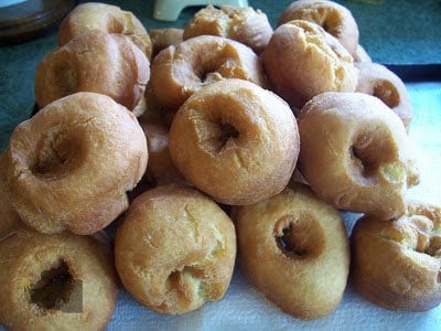 A pile of freshly deep fried buttermilk doughnuts lined on a cookie sheet