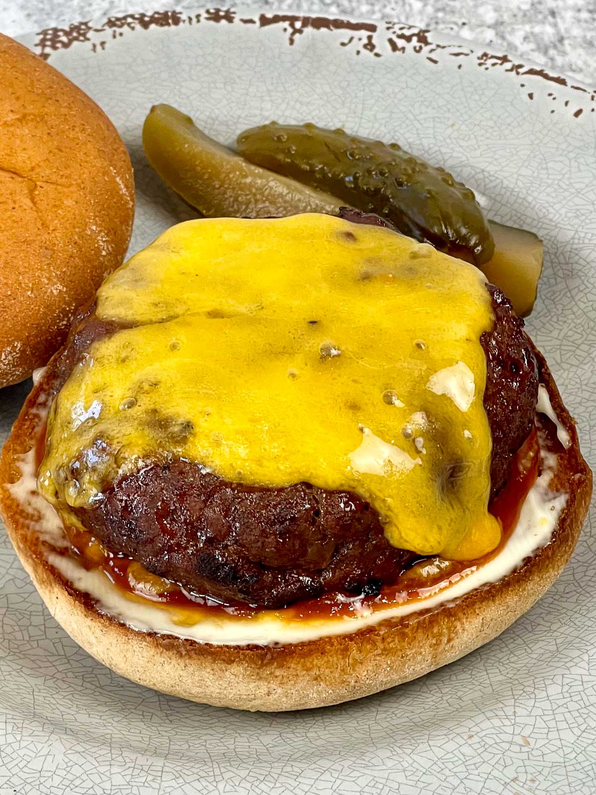 Air Fried Hamburger on a roll topped with cheese and a side of dill pickles.