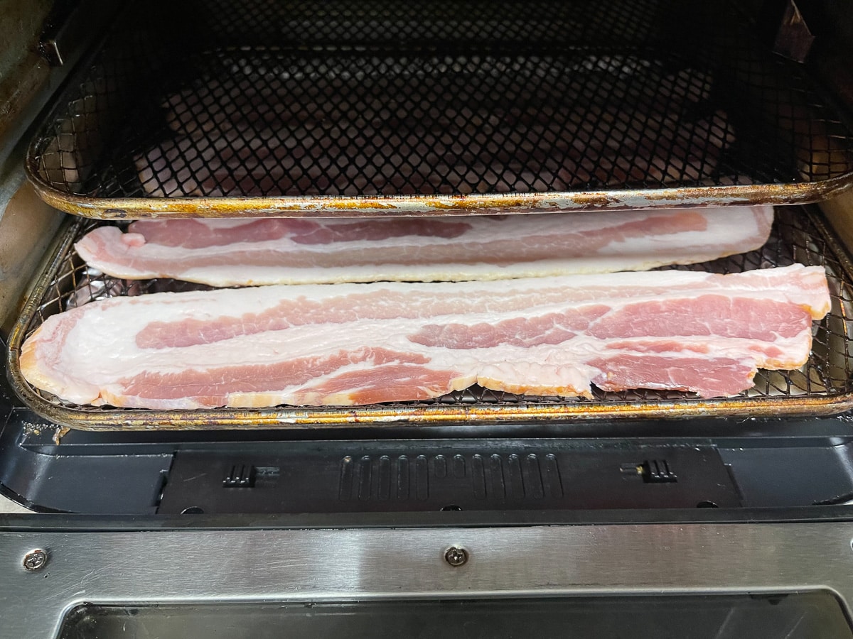 Bacon on air fryer tray on bottom rack of air fryer with a 2nd tray just above the bacon lined tray.