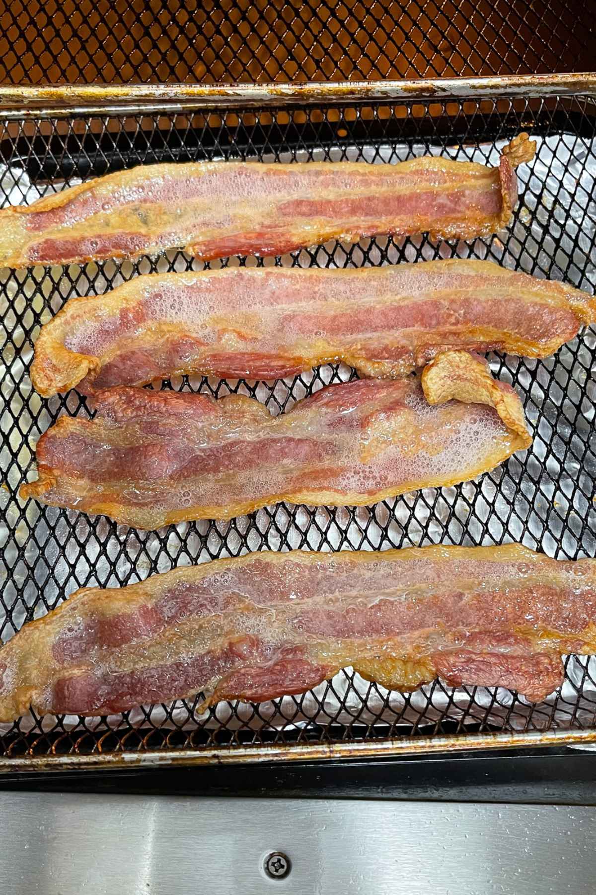 Partially cooked air fryer bacon on air fryer tray.