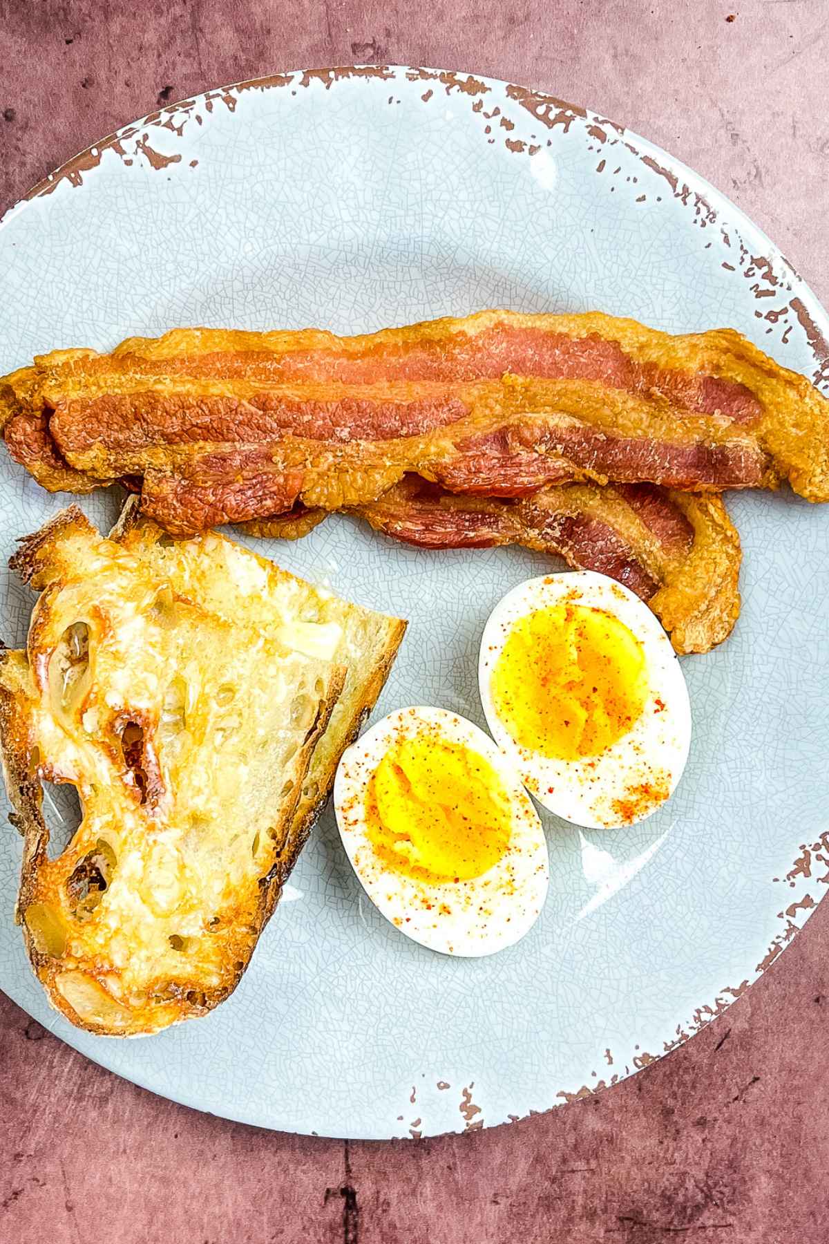 Two slices of bacon on a plate with a halved hard boiled egg and buttered toast.