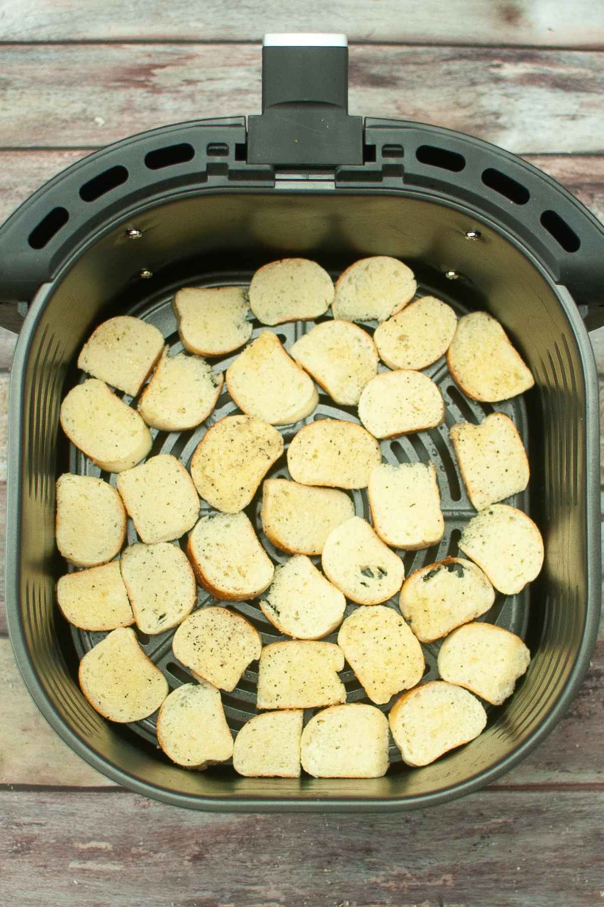 Sliced bagel pieces in air fryer basket before cooking.