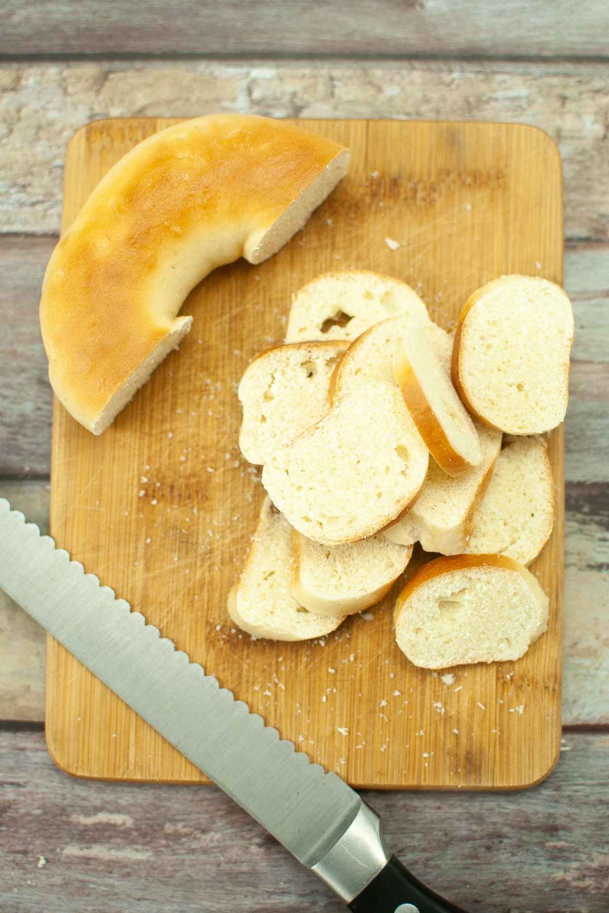 Unsliced bakery bagel on cutting board with chip slices cut from the bagel.