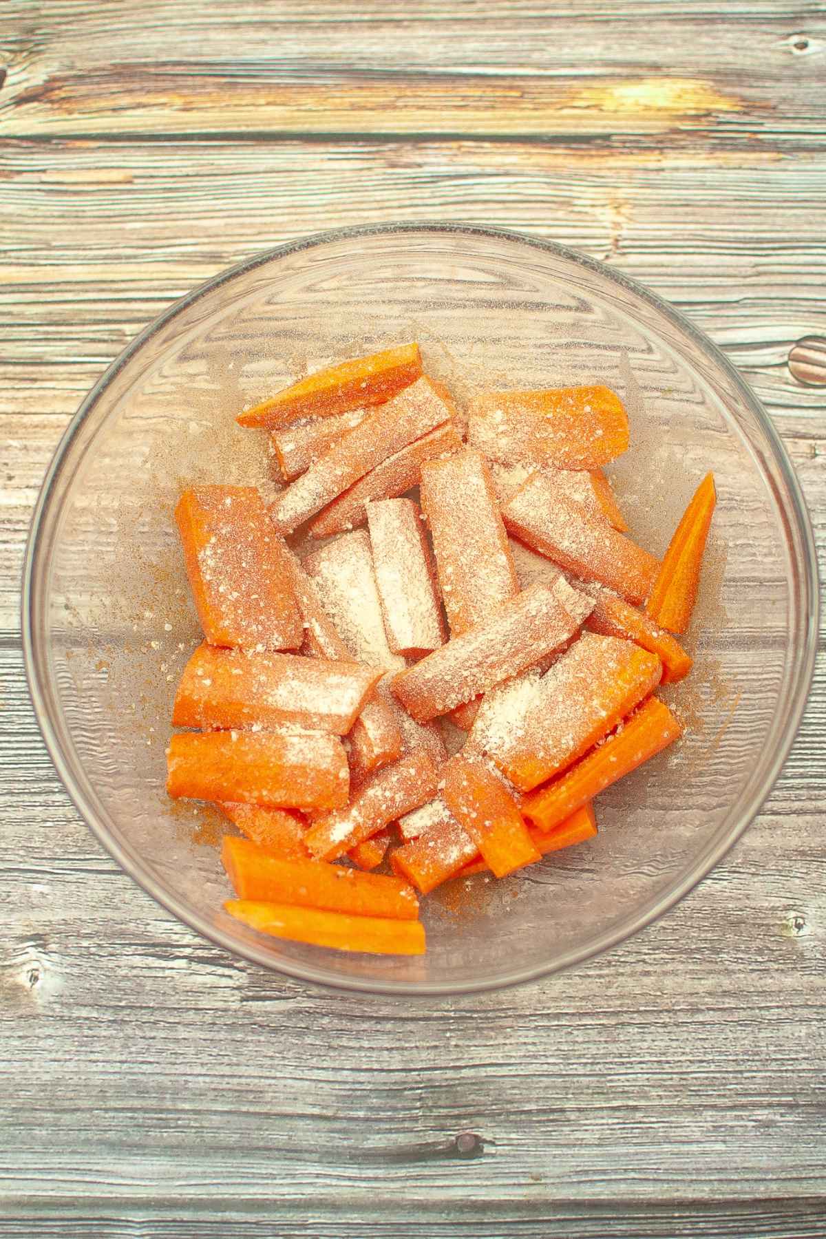 Fresh cut carrots in a glass bowl with seasoning sprinkled on top.