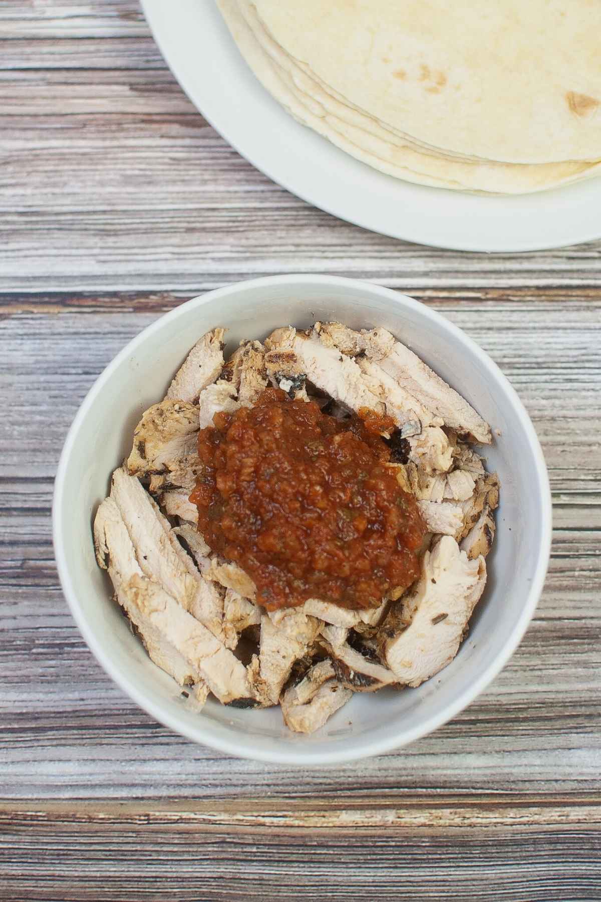 Salsa on top of chicken strips in a white bowl.
