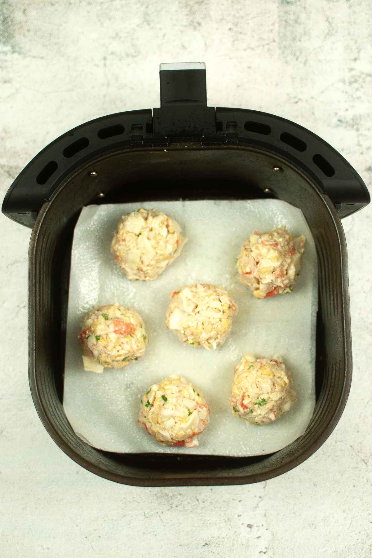 Uncooked crab cakes in air fryer basket lined with parchment paper.