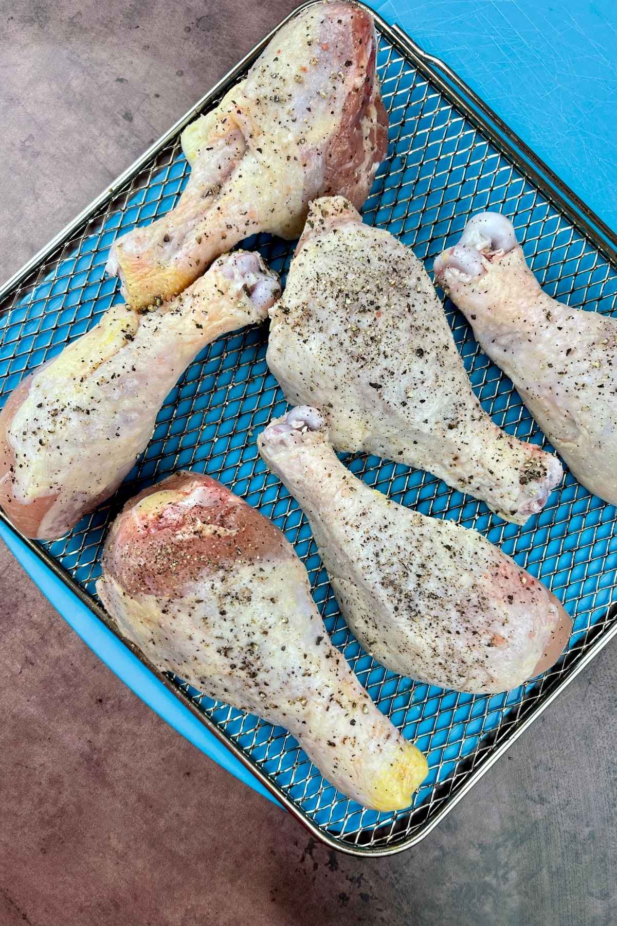 Raw seasoned chicken on an air fryer tray.