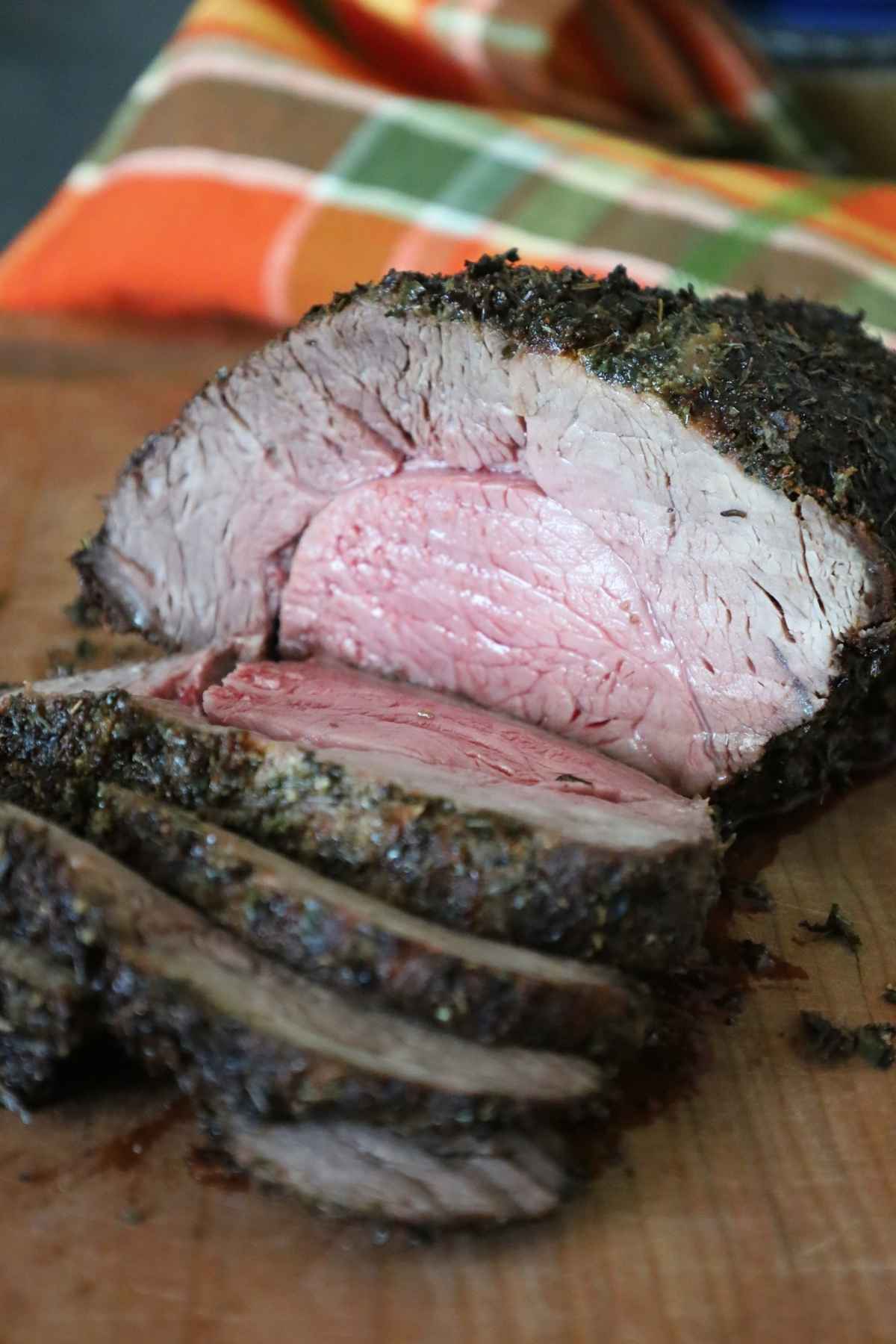 Herb crusted air fryer roast beef on a wooden cutting board with slices cut away from the roast.