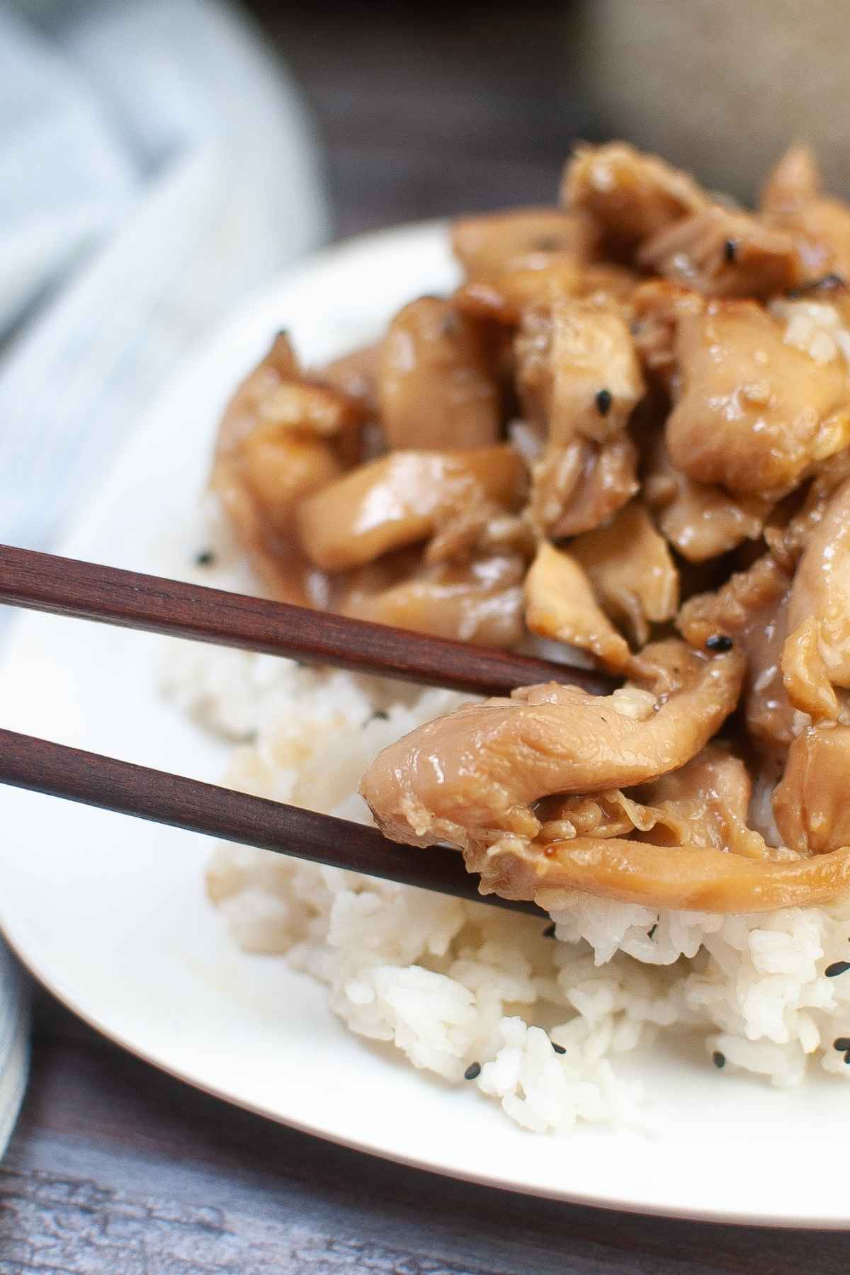 Upclose image of a piece of chicken held with chopsticks.