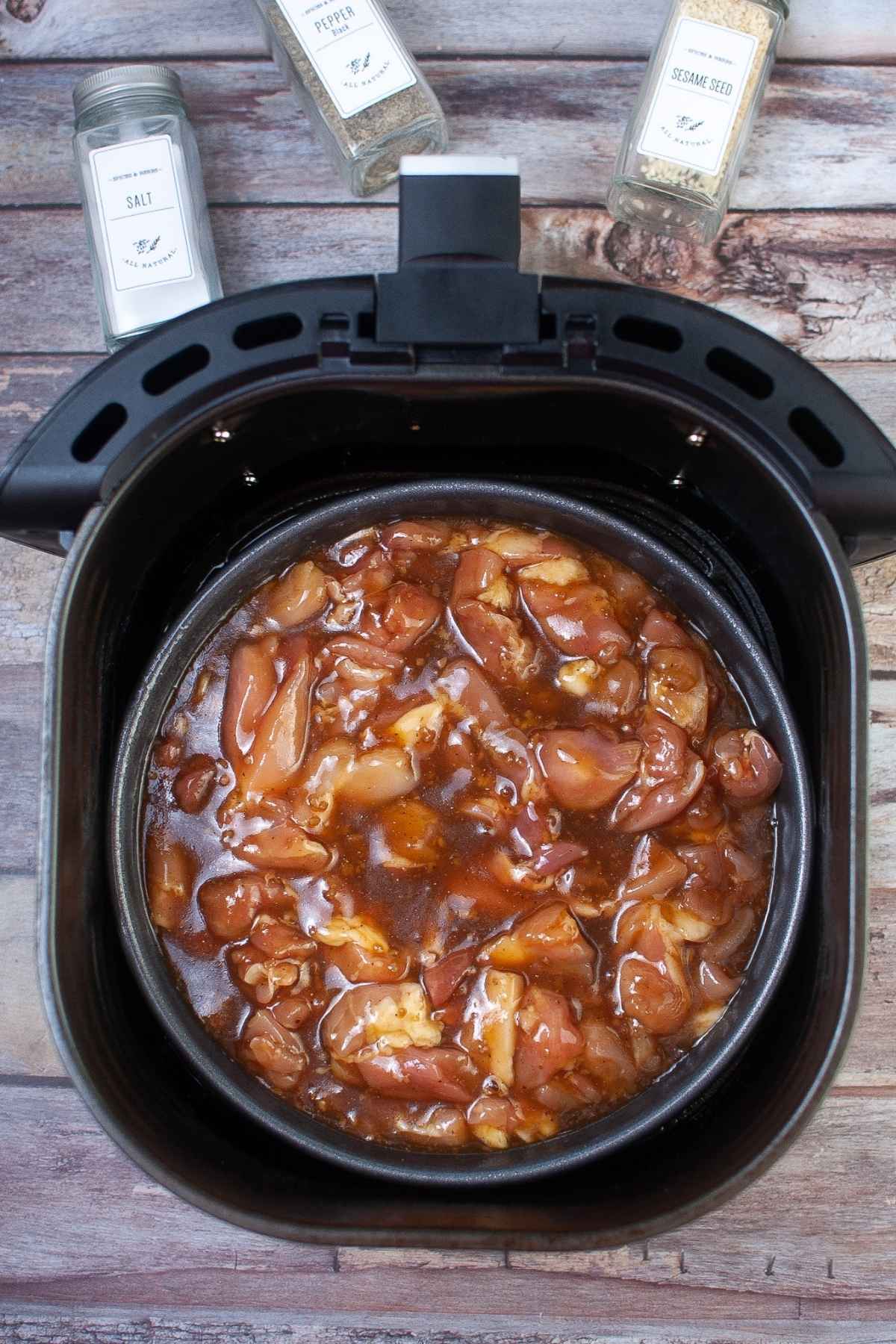 Raw chicken with sauce in pan inside of air fryer