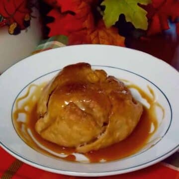 A golden brown baked apple dumpling on a cream bowl drizzled with salted caramel rum sauce.