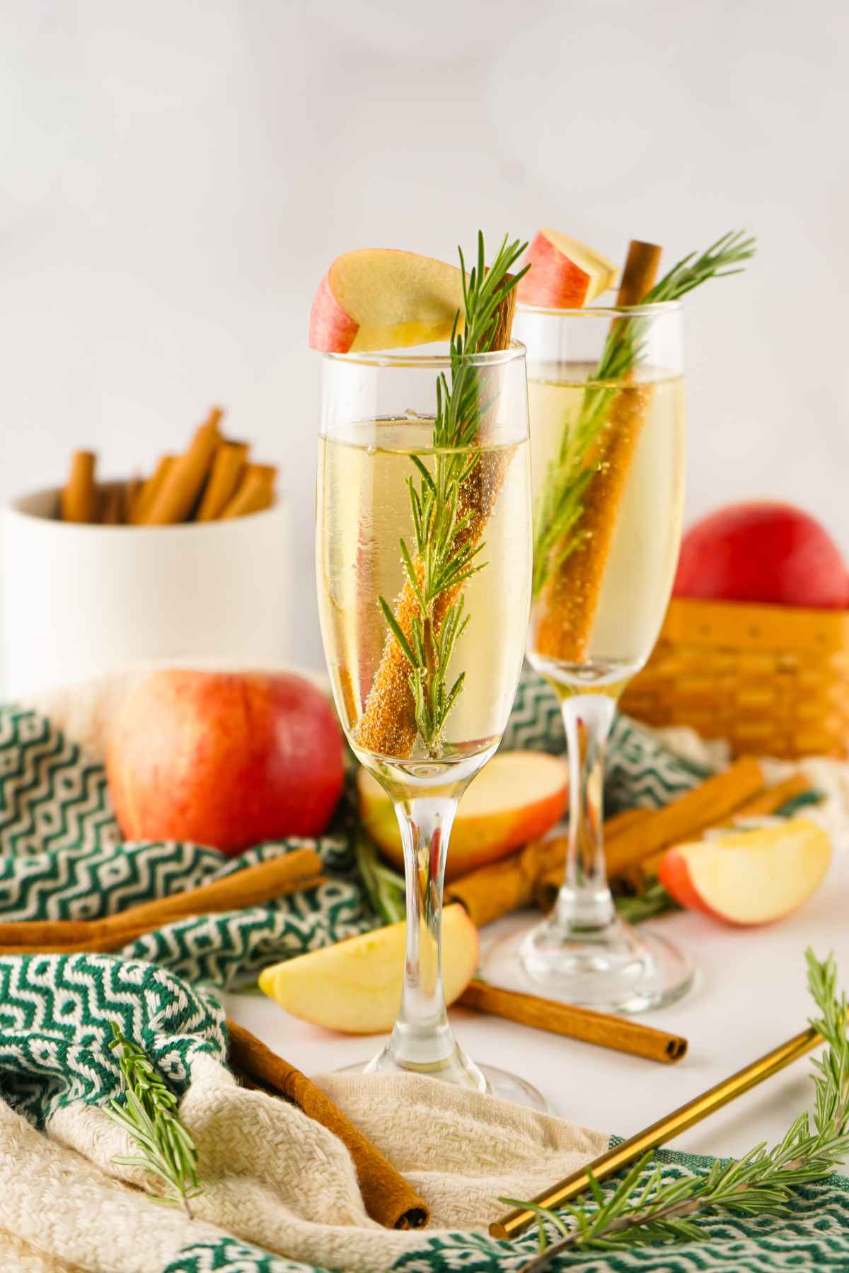 Two Apple Cider Mimosa with apple slice, rosemary twig, and cinnamon stick garnish.