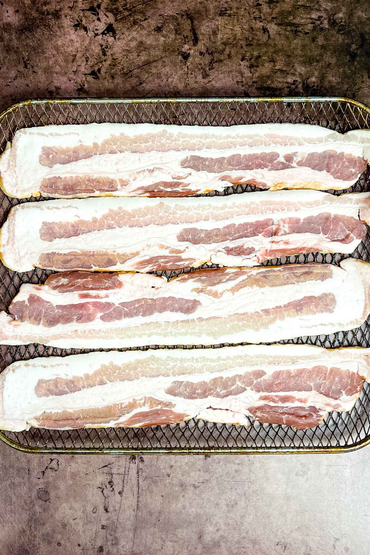 Raw bacon slices on air fryer tray.