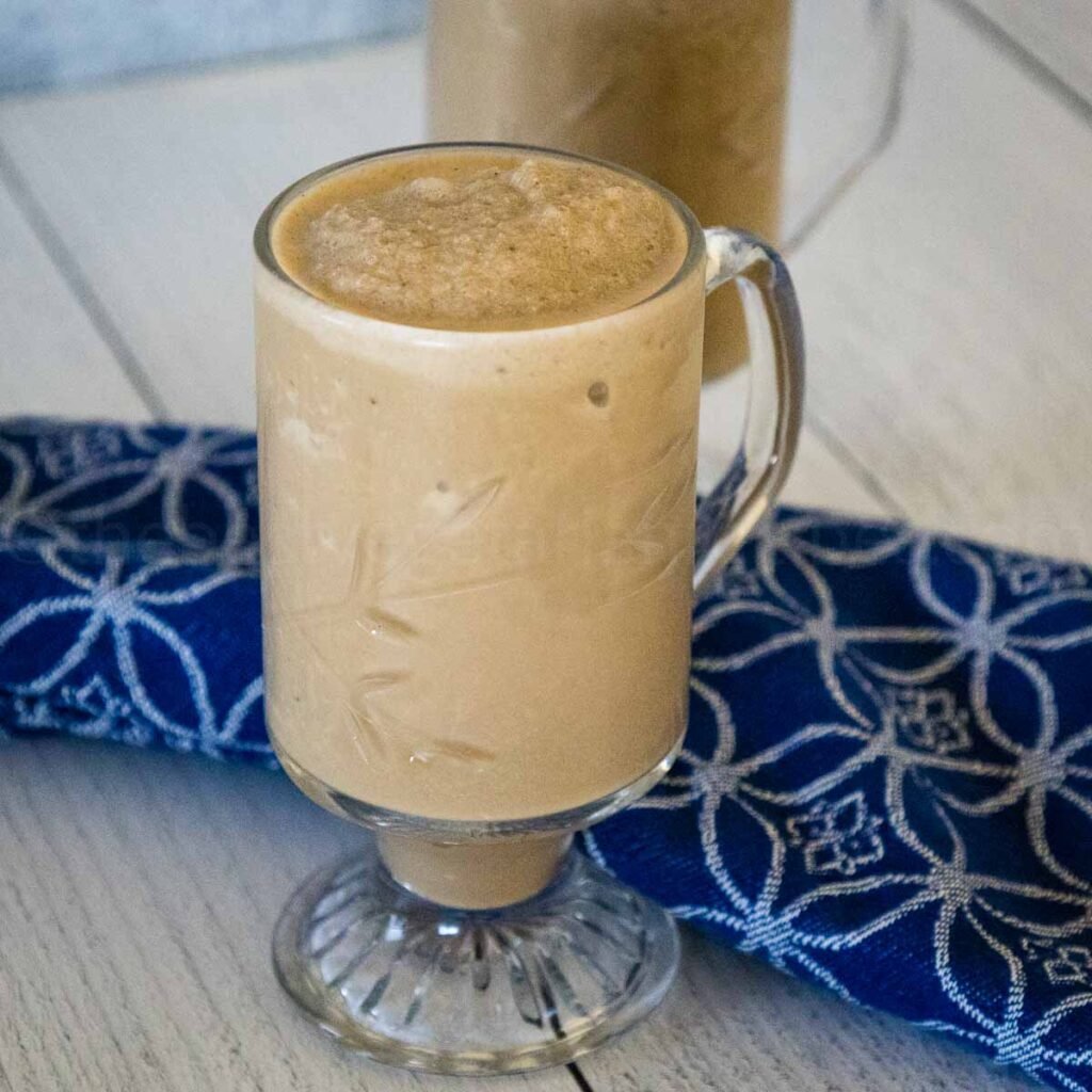 Banana Coffee Smoothie in a crystal mug with a blue and white napkin blurred in the background.