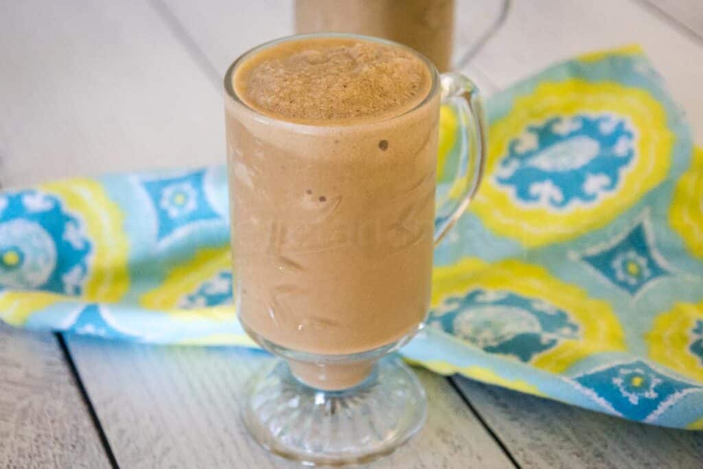 Banana Coffee Smoothie in a clear glass footed mug with a blue and yellow napkin the background.