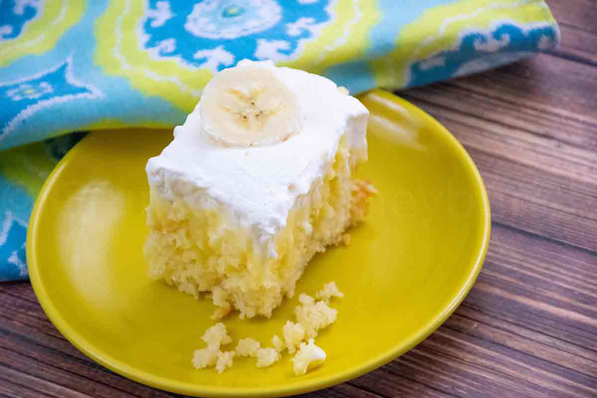 Banana Cream Poke Cake on a yellow plate with a blue and yellow napkin in the background.