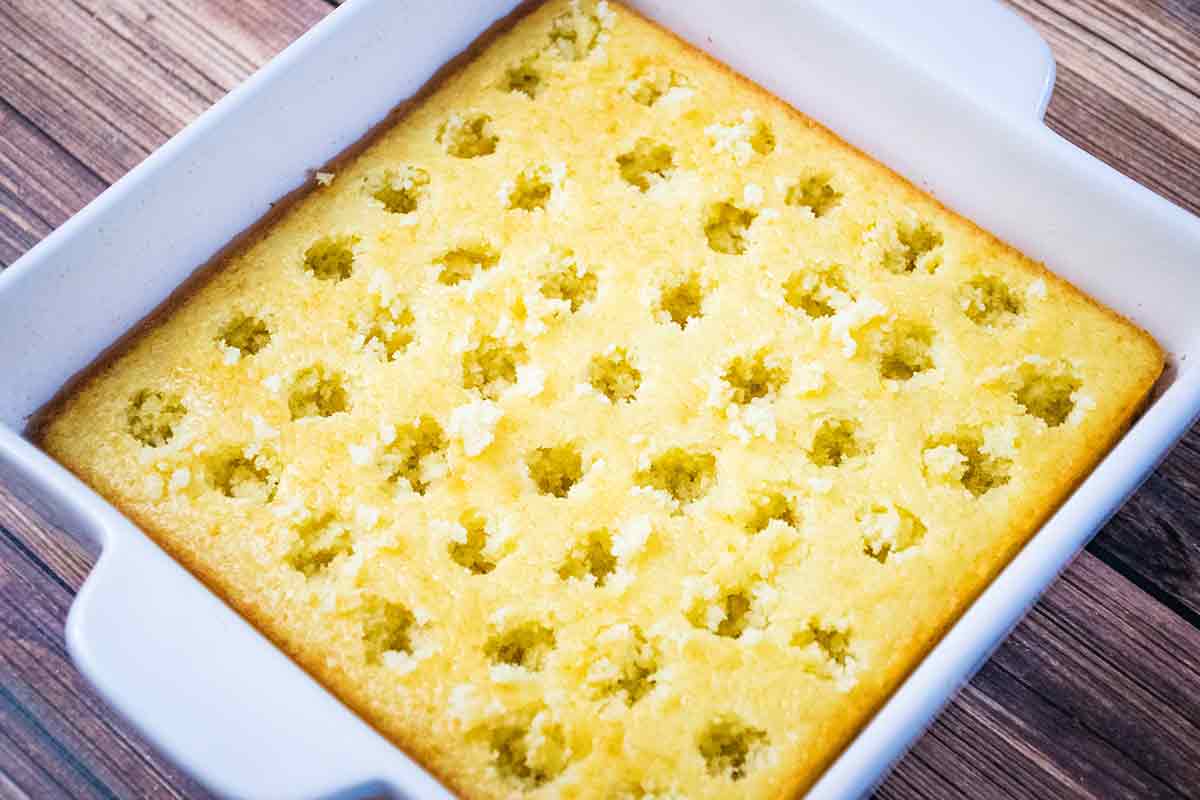 Yellow cake in a white ceramic baking dish with large holes over the surface of the cake.