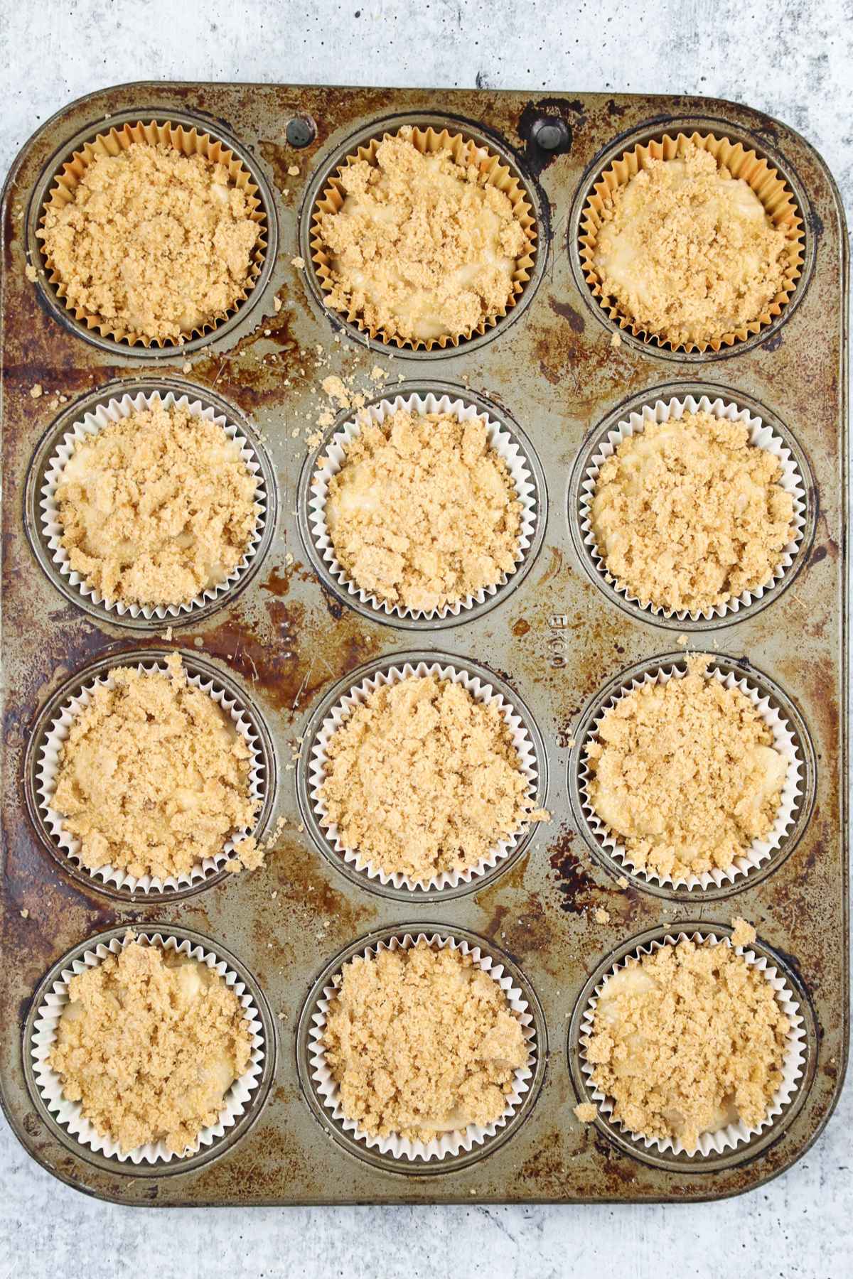 Muffin batter in tin with crumb topping before baking.