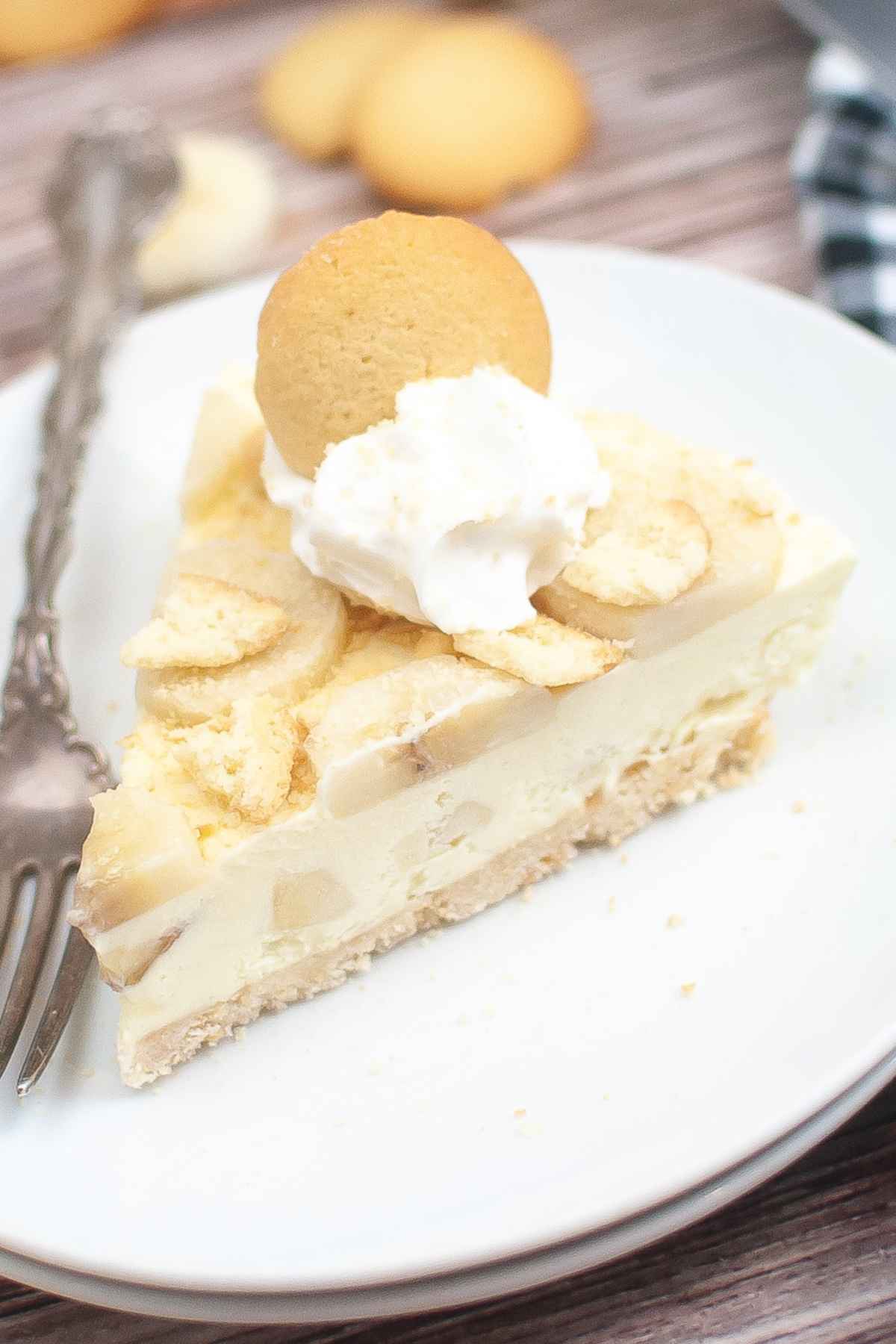 Hero image of banana pudding cheesecake topped with whipped cream and a vanilla wafer cookie on a white plate.