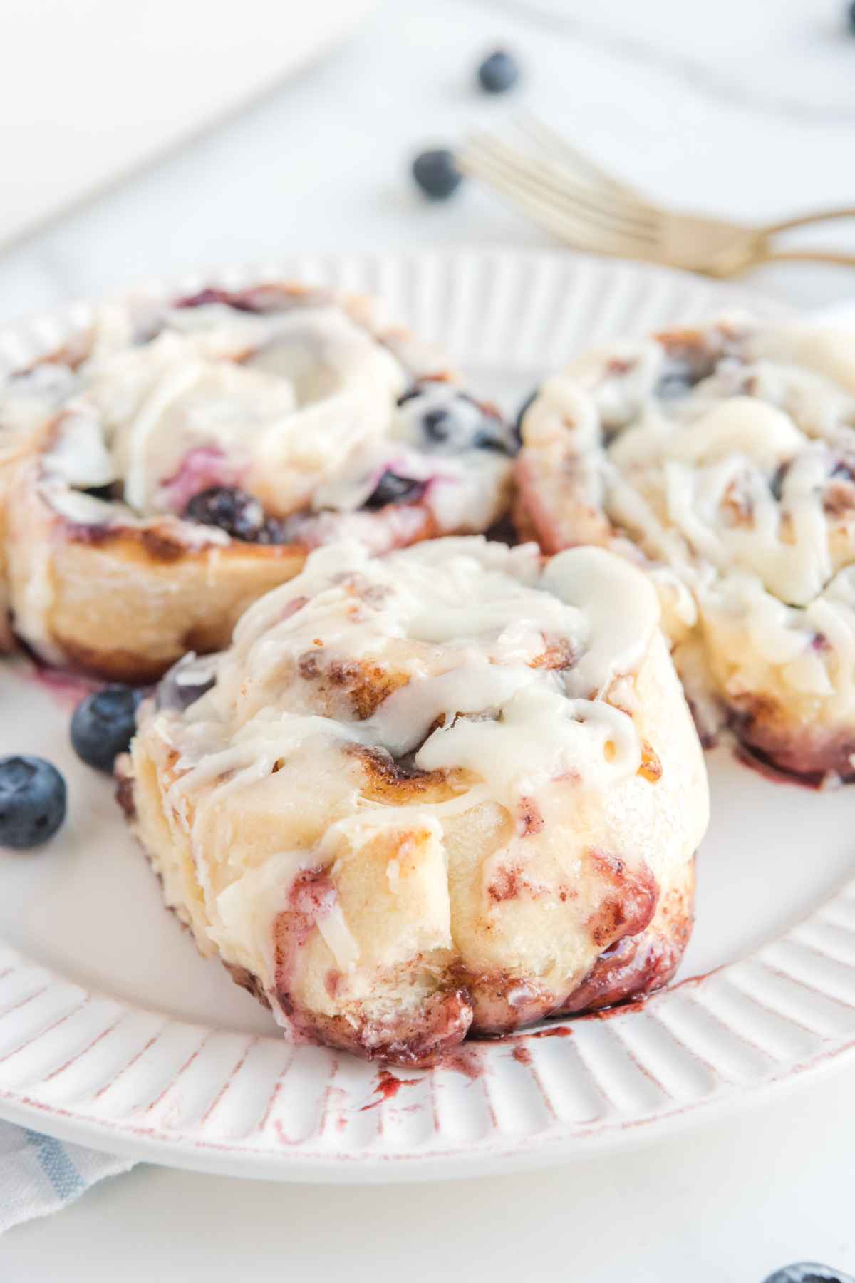 Side view of blueberry cinnamon rolls on a white plate.