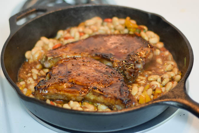 Bourbon glazed Pork chops in a cast iron skillet surrounded by beans.