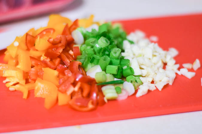 Diced peppers, garlic, and onions on a red cutting board.