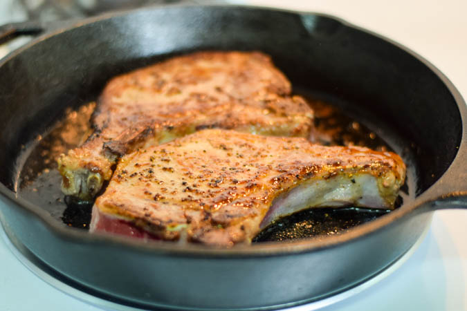 Pork chops cooking in a cast iron skillet.