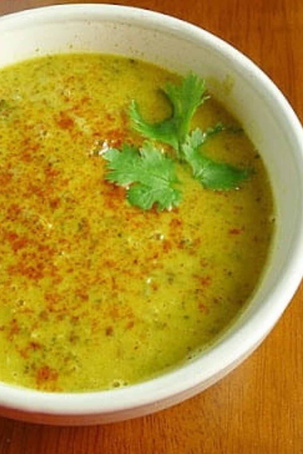 A white bowl filled with broccoli dal and garnished with cilantro and cayenne pepper.