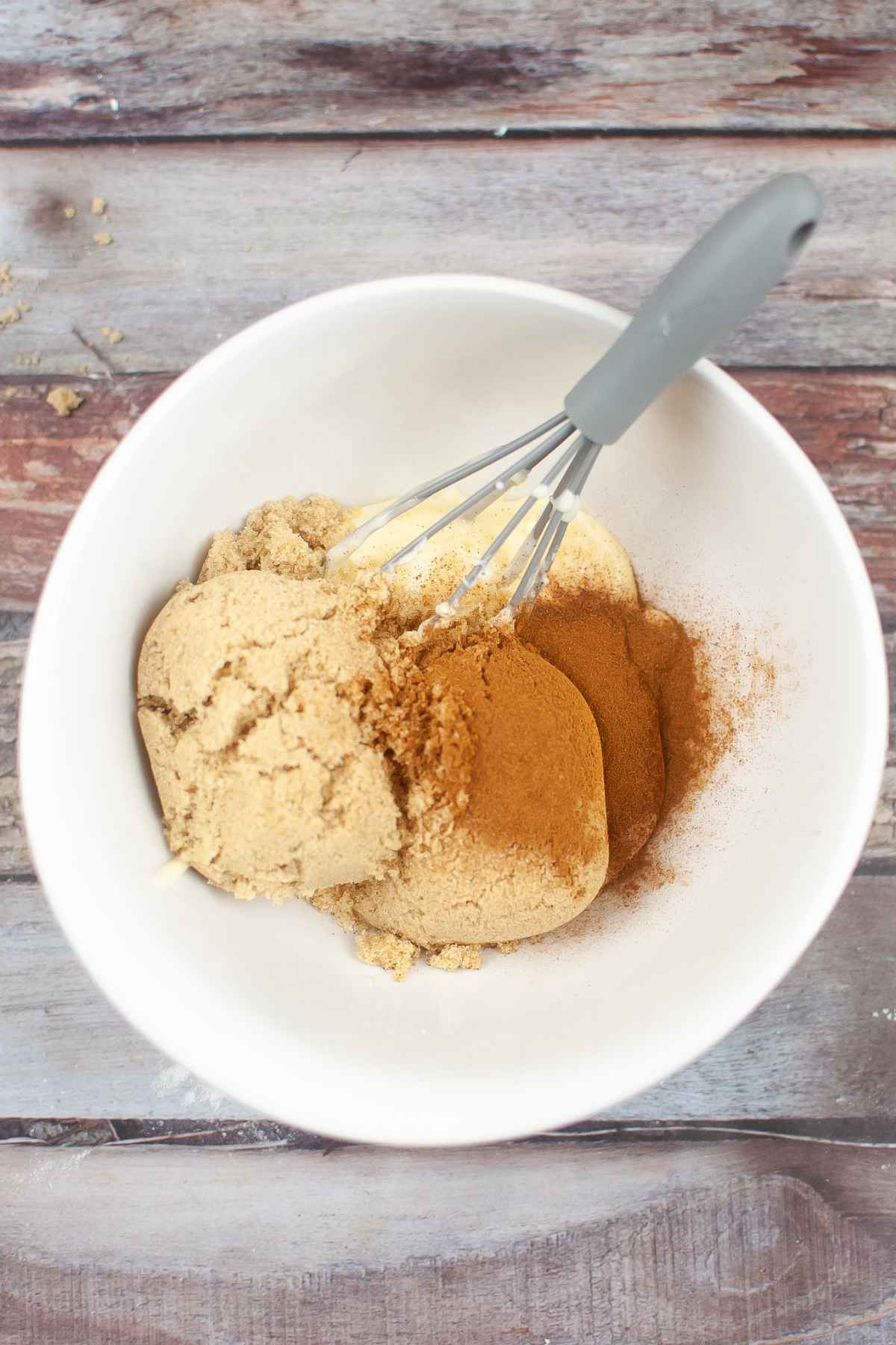 Brown sugar, butter, and cinnamon in a white mixing bowl with a hand whisk.