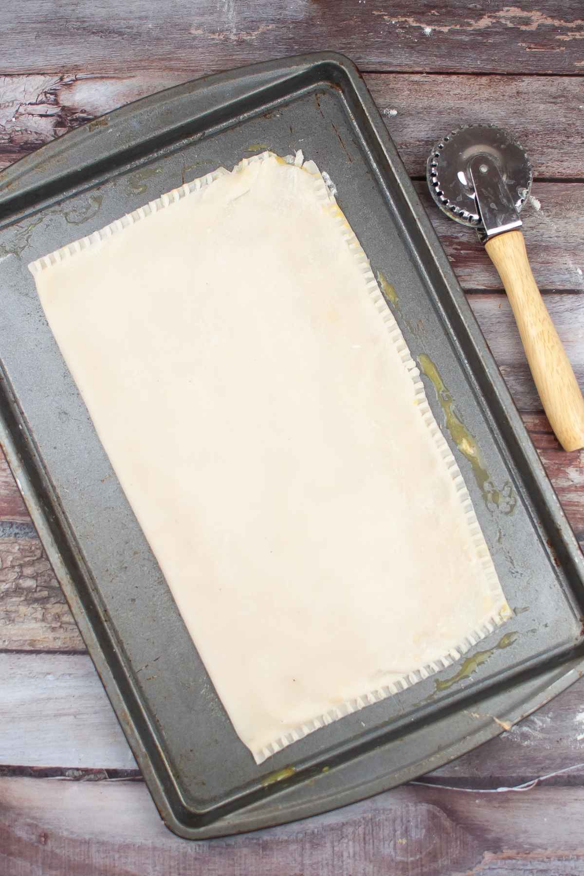 Unbaked poptart on baking sheet with edges crimped and crimper laying beside the baking sheet.