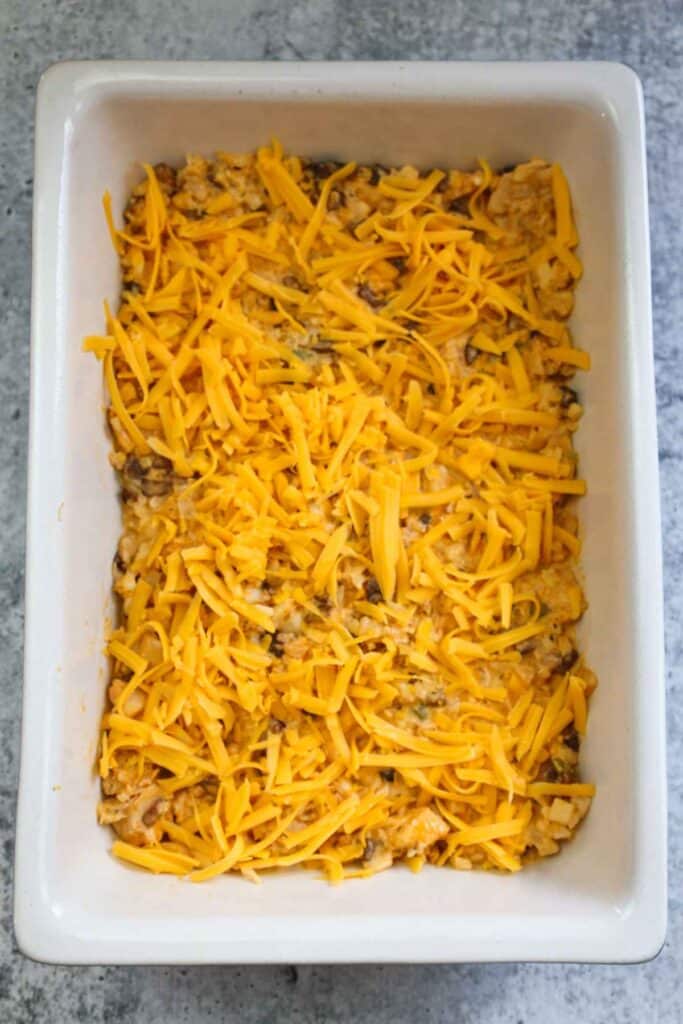 Unbaked casserole topped with shredded cheese.