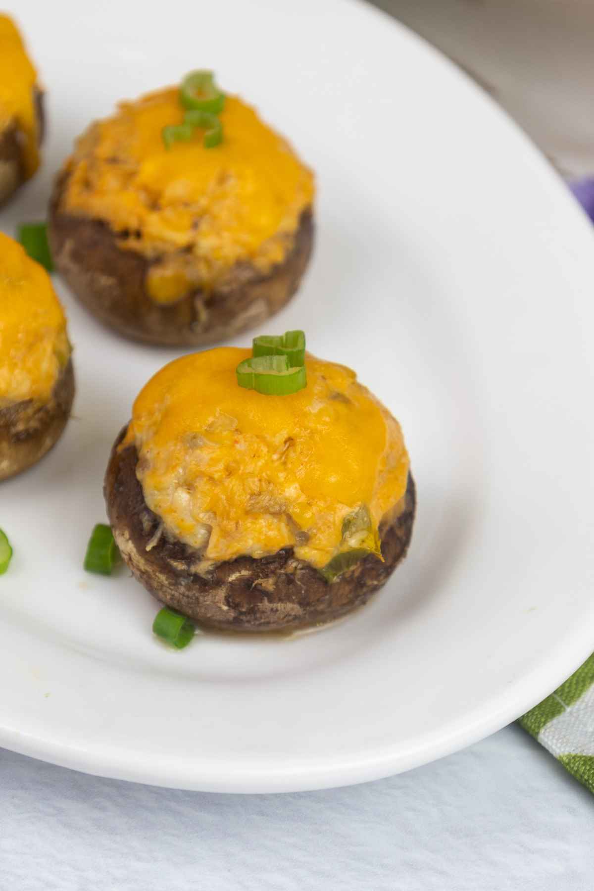 Baked buffalo chicken stuffed mushrooms on a white plate garnished with green onion tops.