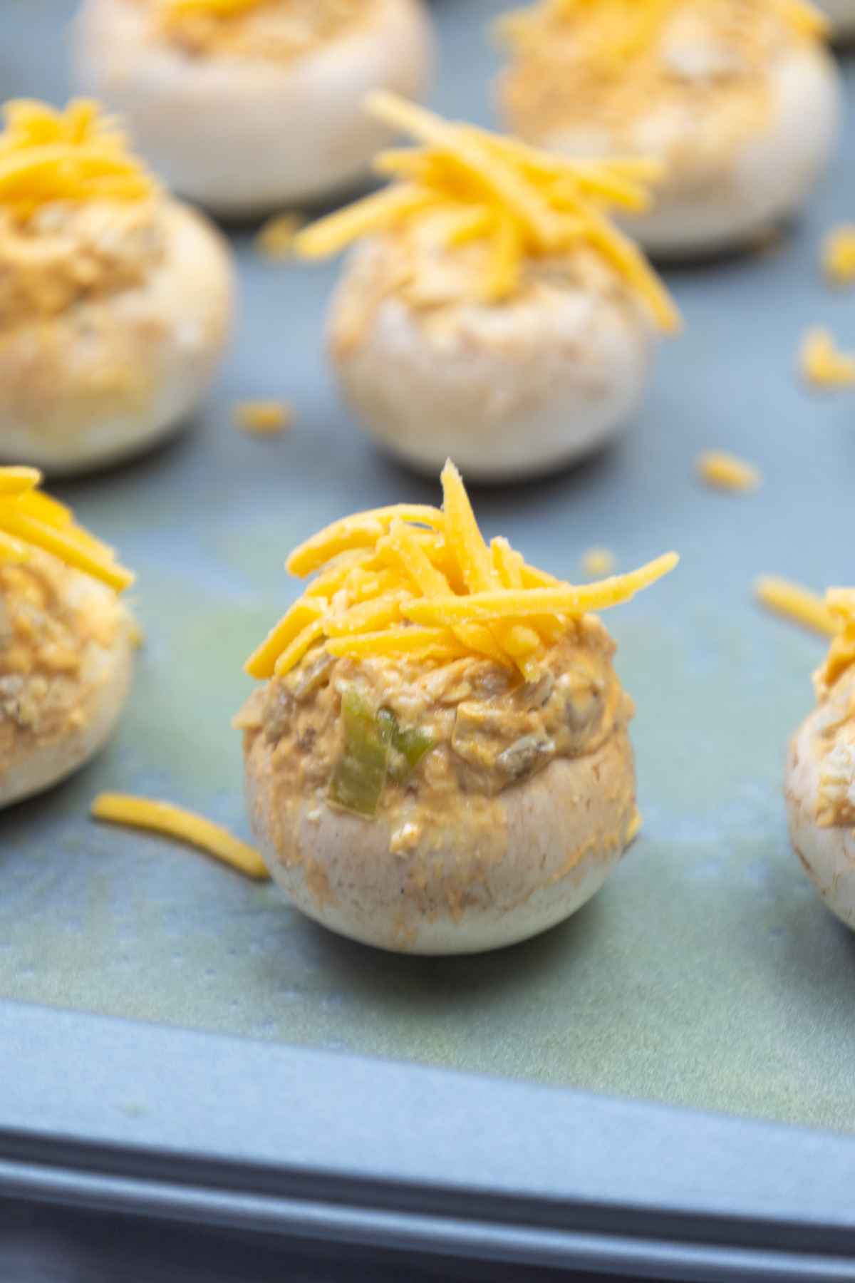Image of an unbaked mushroom topped with cheese on the baking sheet.