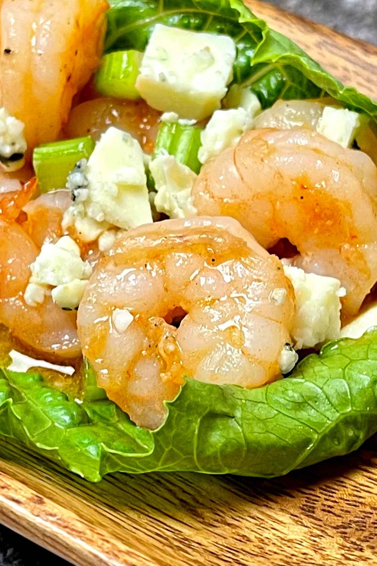 Up close image of cooked shrimp coated in buffalo sauce with blue cheese and celery.