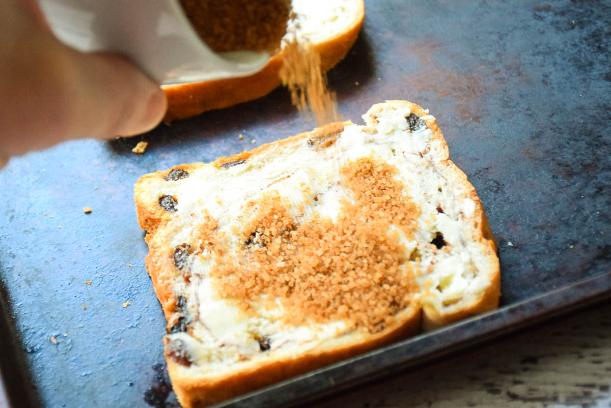 Sprinkling sugar mixture over top of buttered raisin bread.