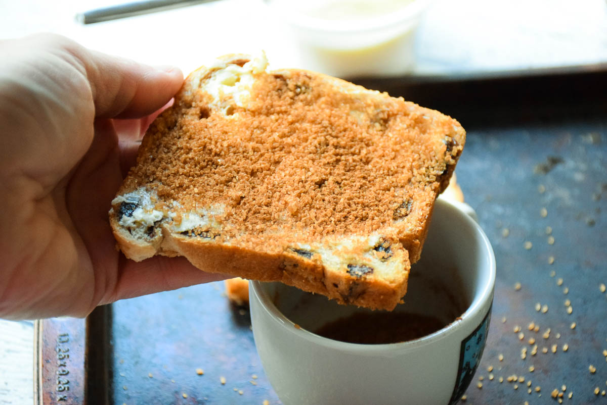 A hand holding a piece of bread with cinnamon and sugar mixture on top.