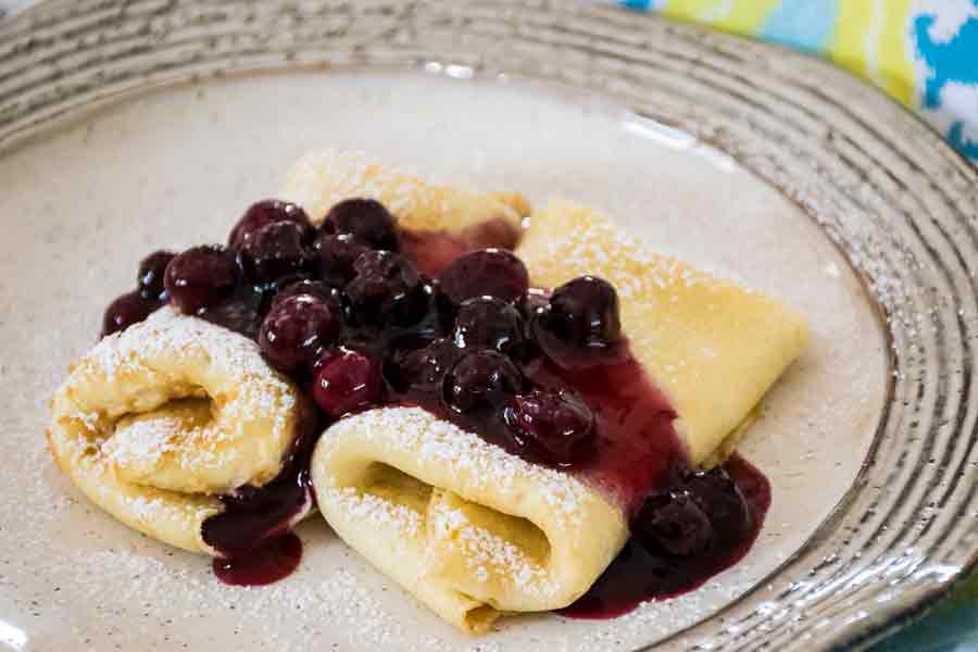 Two cheese blintzes on a plate with blueberry sauce.
