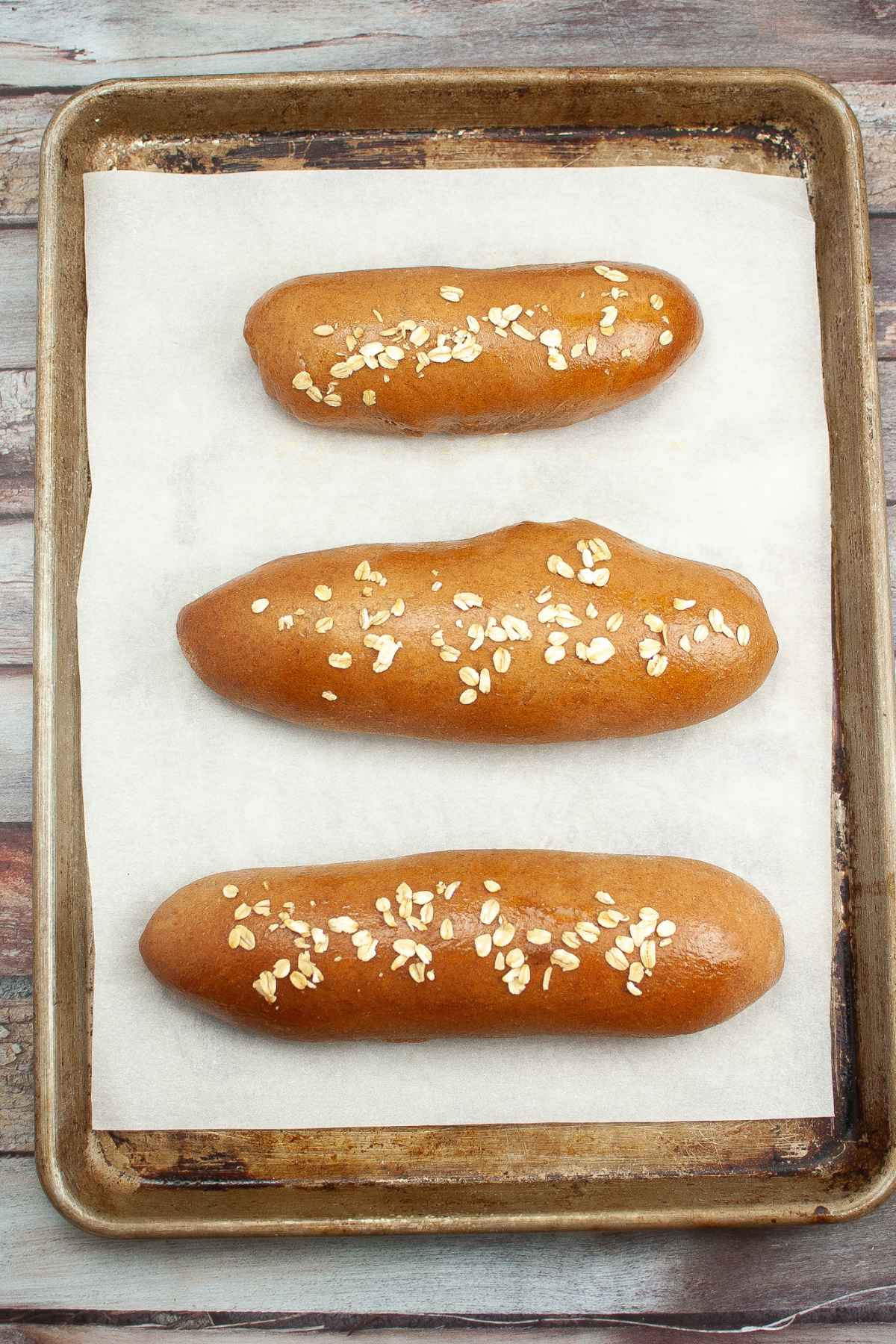 Three loaves of baked cheesecake factory brown bread on a parchment lined baking sheet.