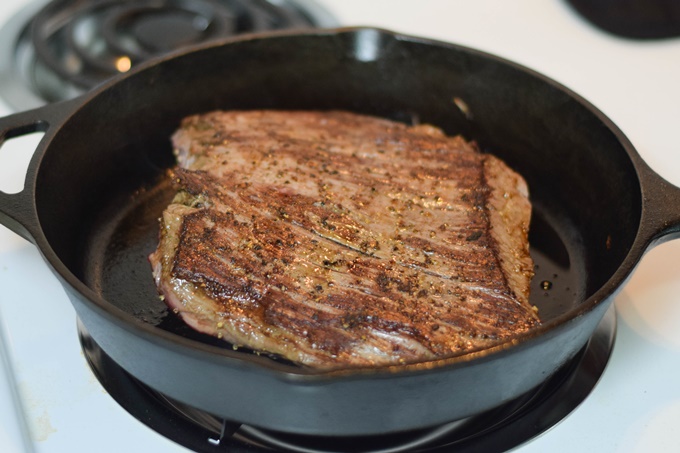 A seared flank steak in a cast iron skillet.