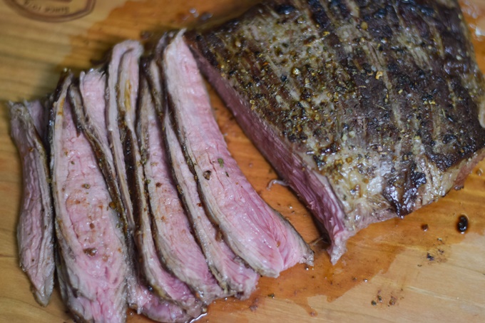 Sliced medium rare flank steak on a cutting board.