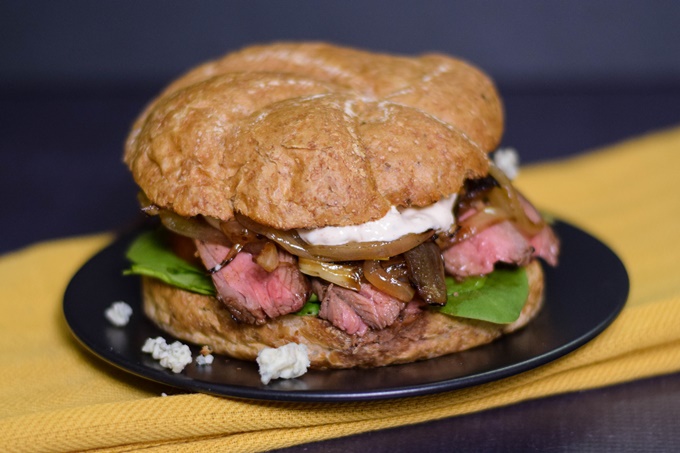 Thin slices of steak sandwiched with a whole wheat bun with caramelized onion and blue cheese sauce topping.