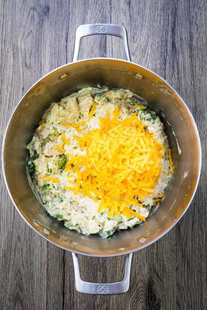 Overhead image of mixed casserole with shredded cheese on top before mixing in.