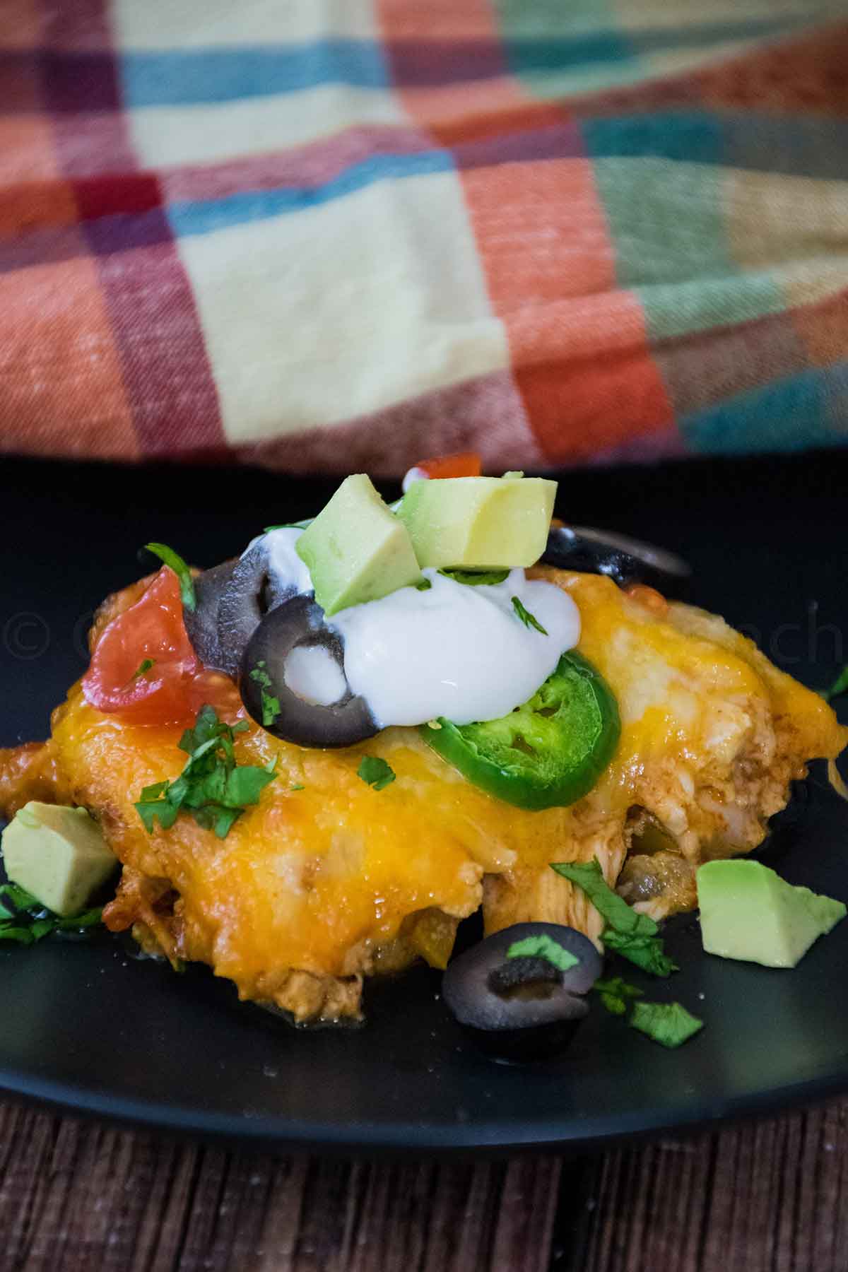 A serving of low carb chicken enchilada casserole topped with olives, sour cream, avocado, and cilantro on a black plate.