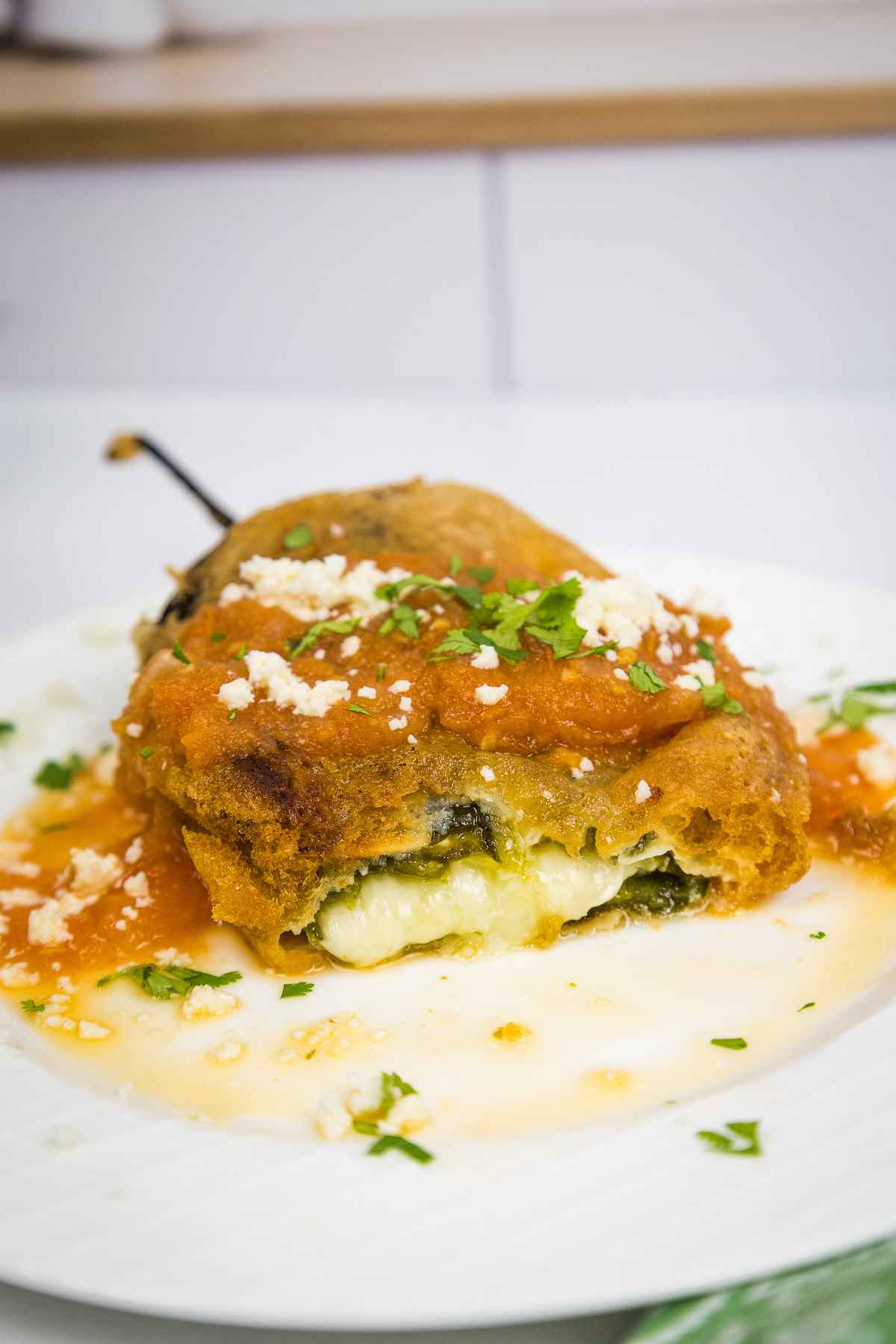 Chile Relleno on a plate with a portion cut from the chile and cheese oozing out.