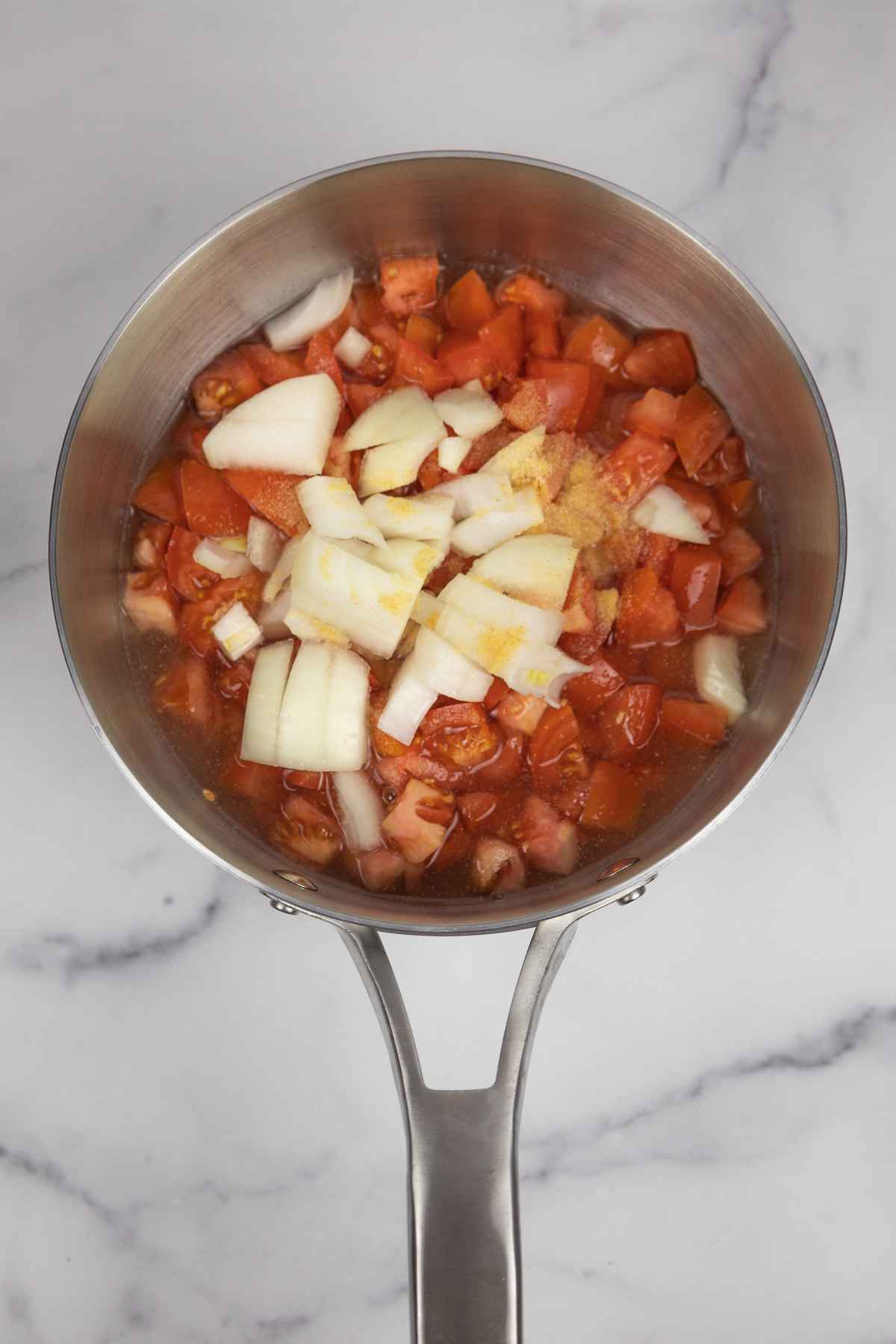 Tomatoes, onion, and garlic powder in a saucepan.