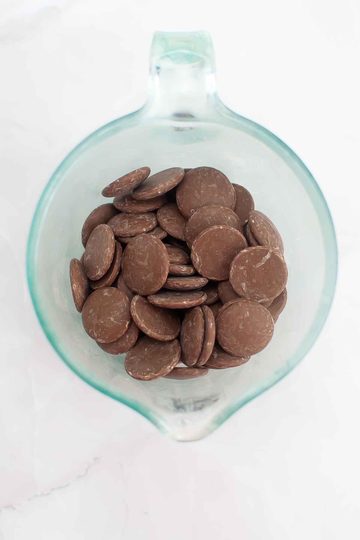 Milk chocolate candy melts in a clear glass measuring cup.