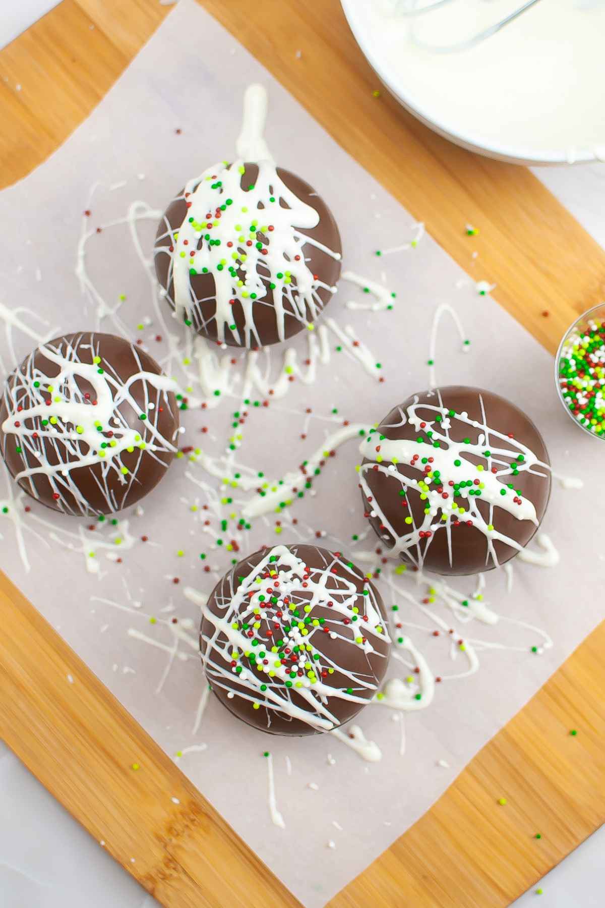 Four hot chocolate bombs on parchment paper with white chocolate drizzle over top.