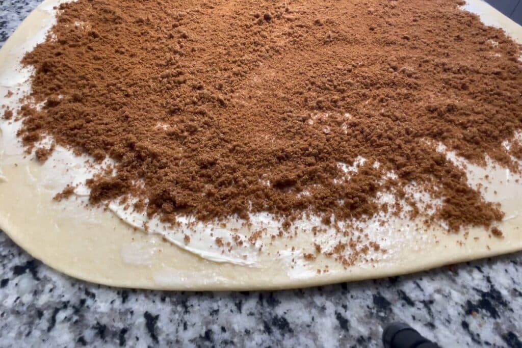 Cinnamon roll dough with cinnamon sugar filling on top of the buttered dough.