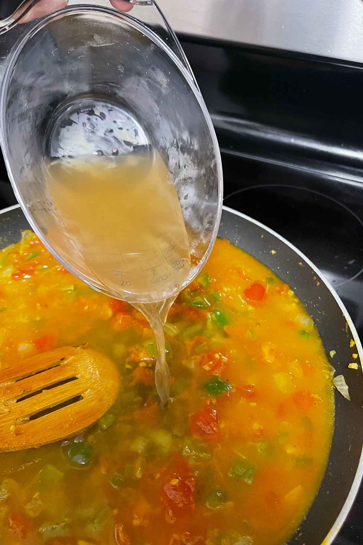 Pouring chicken broth into the cooked vegetables.