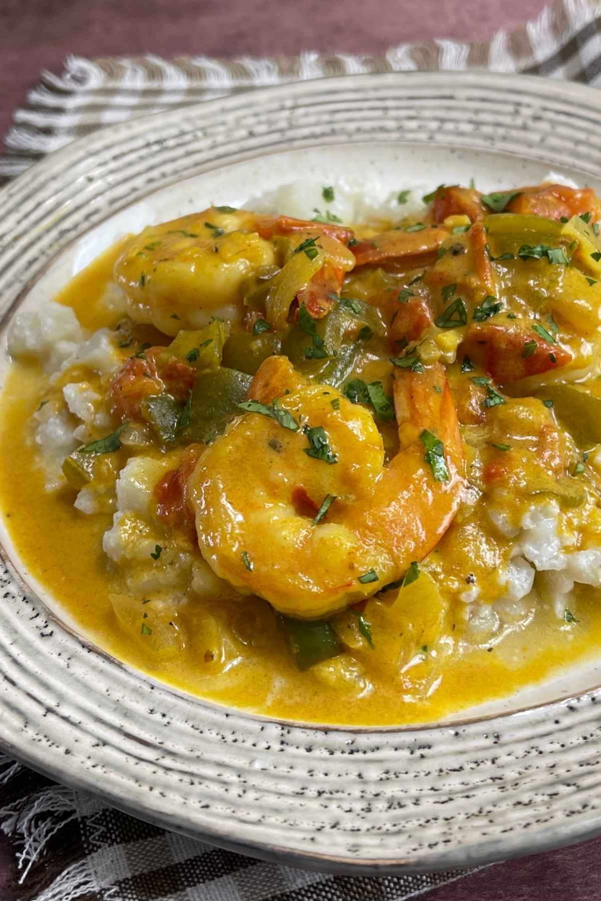 A plate with shrimp in a curry sauce on top of coconut cauliflower rice.